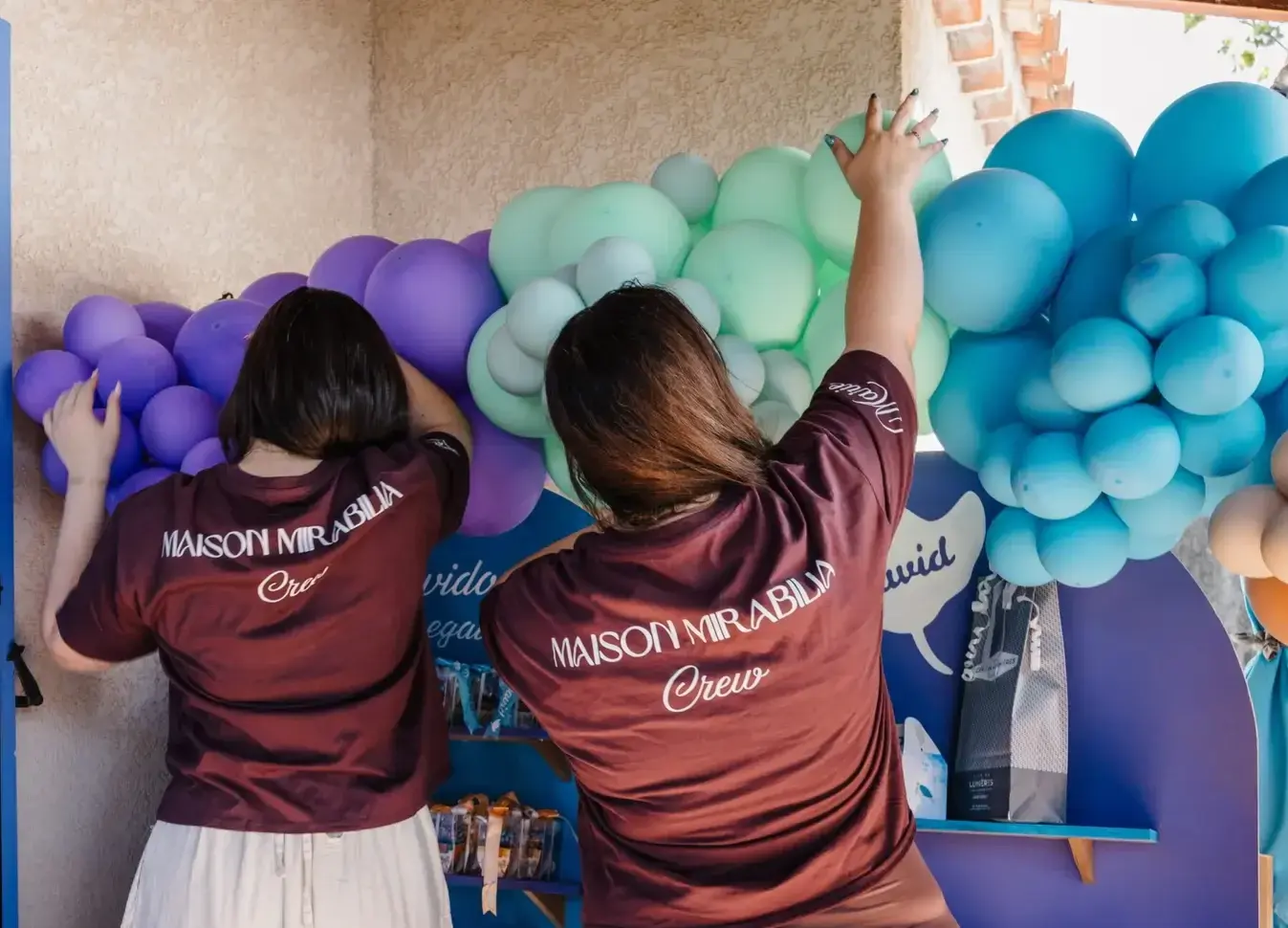 Twee mensen in shirts met Maison Mirabilia Crew op de rug bouwen een ballonwand op