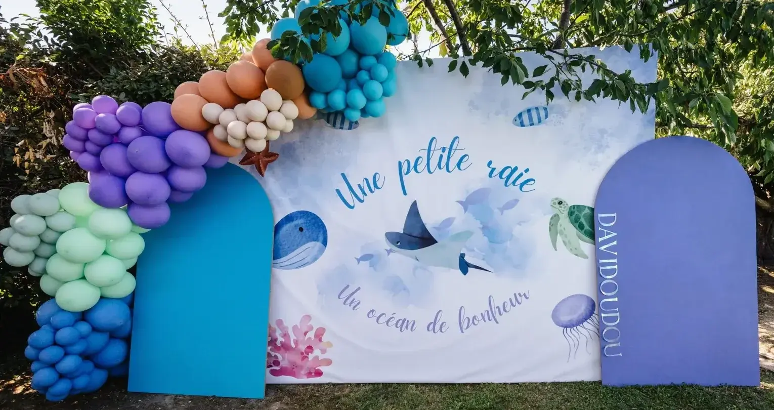 Ballonboog in pastelgroen, lila en blauw voor een witte achterwand met zeedieren en de tekst Un océan de bonheur